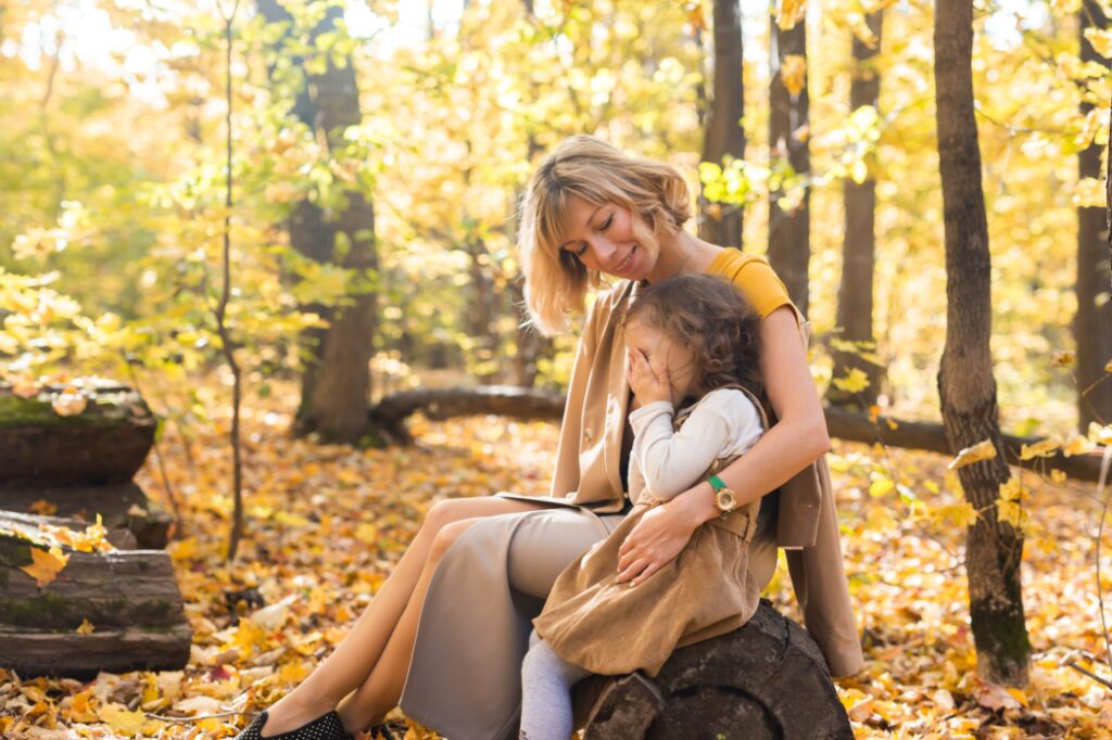 Mother comforting her crying little girl in autumn nature. Emotions and family concept